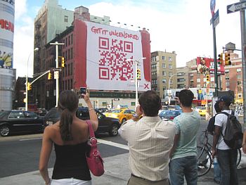 A group of people using smartphones to scan a billboard-sized Quick Response code